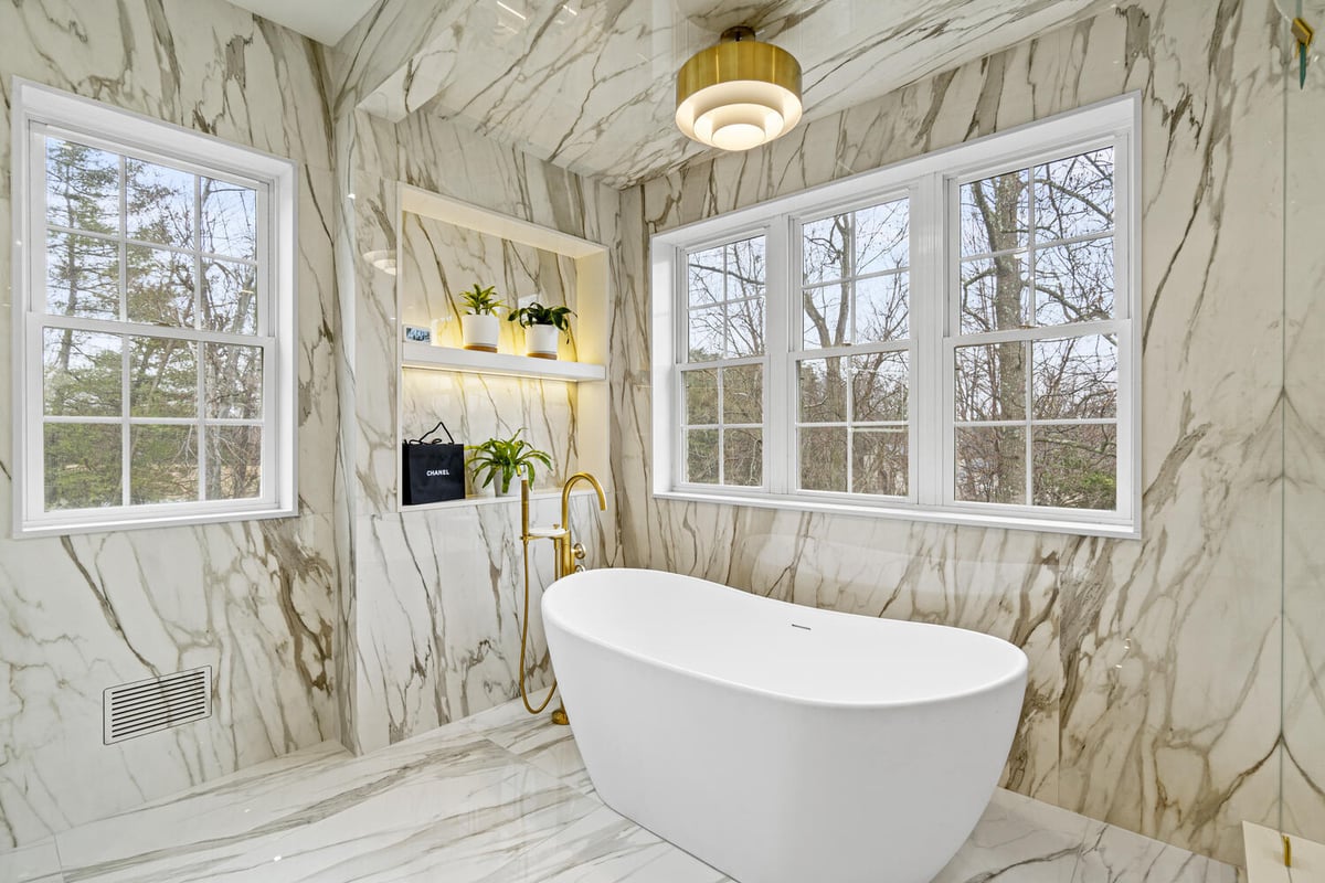 Freestanding tub in marble-wrapped bathroom with gold fixtures by DesignLab in Metro Washington