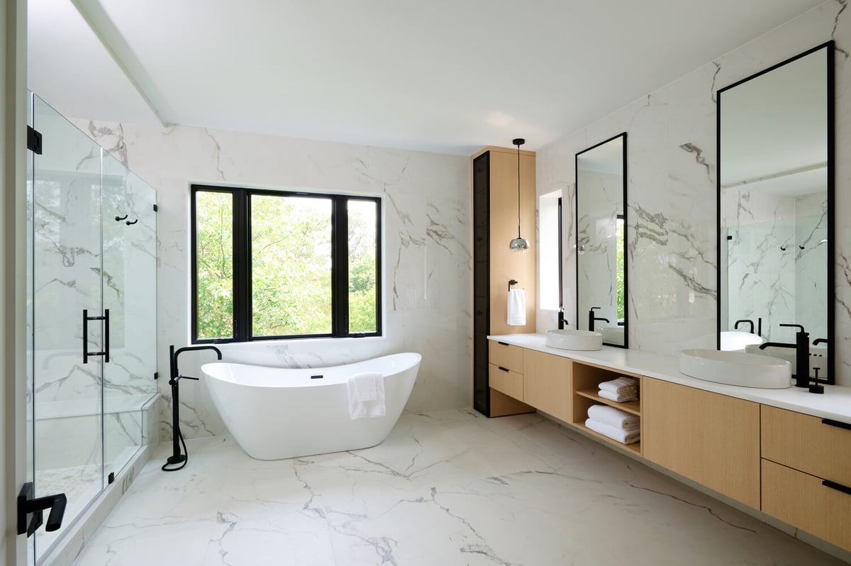 Marble-tiled master bathroom with large mirrors and natural wood cabinetry in a Washington, DC custom home