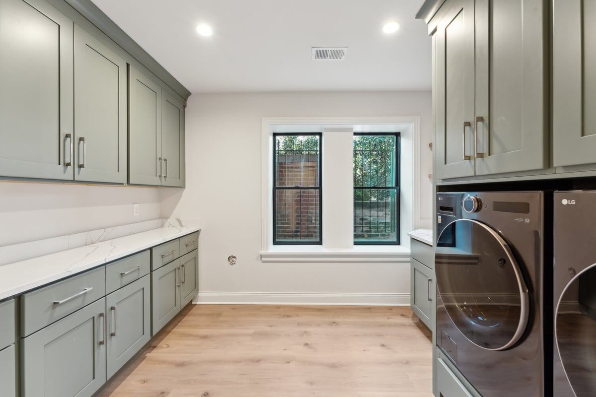 Spacious laundry room with sage green cabinets and front-load appliances in a Rhode Island custom home by DesignLab