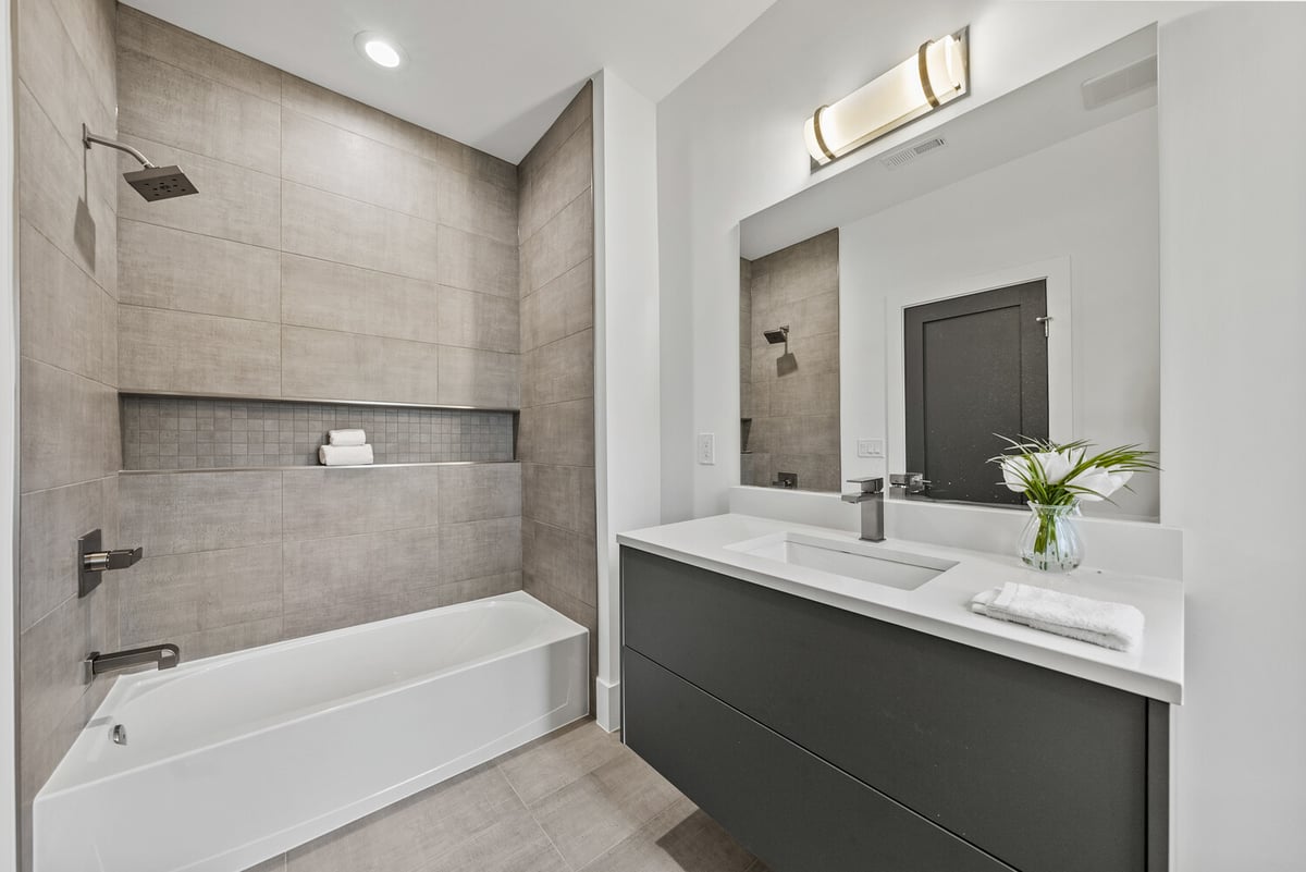 Neutral bathroom with tiled shower and black vanity in River Oaks whole home by DesignLab